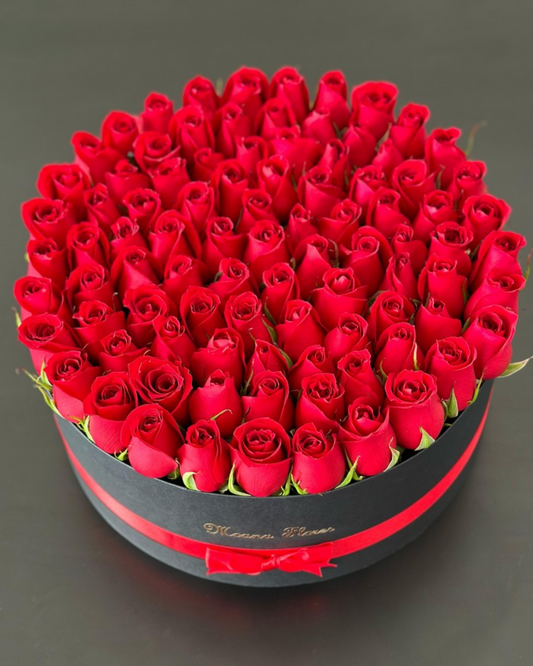Rosas rojas en caja circular negra y listón rojo.