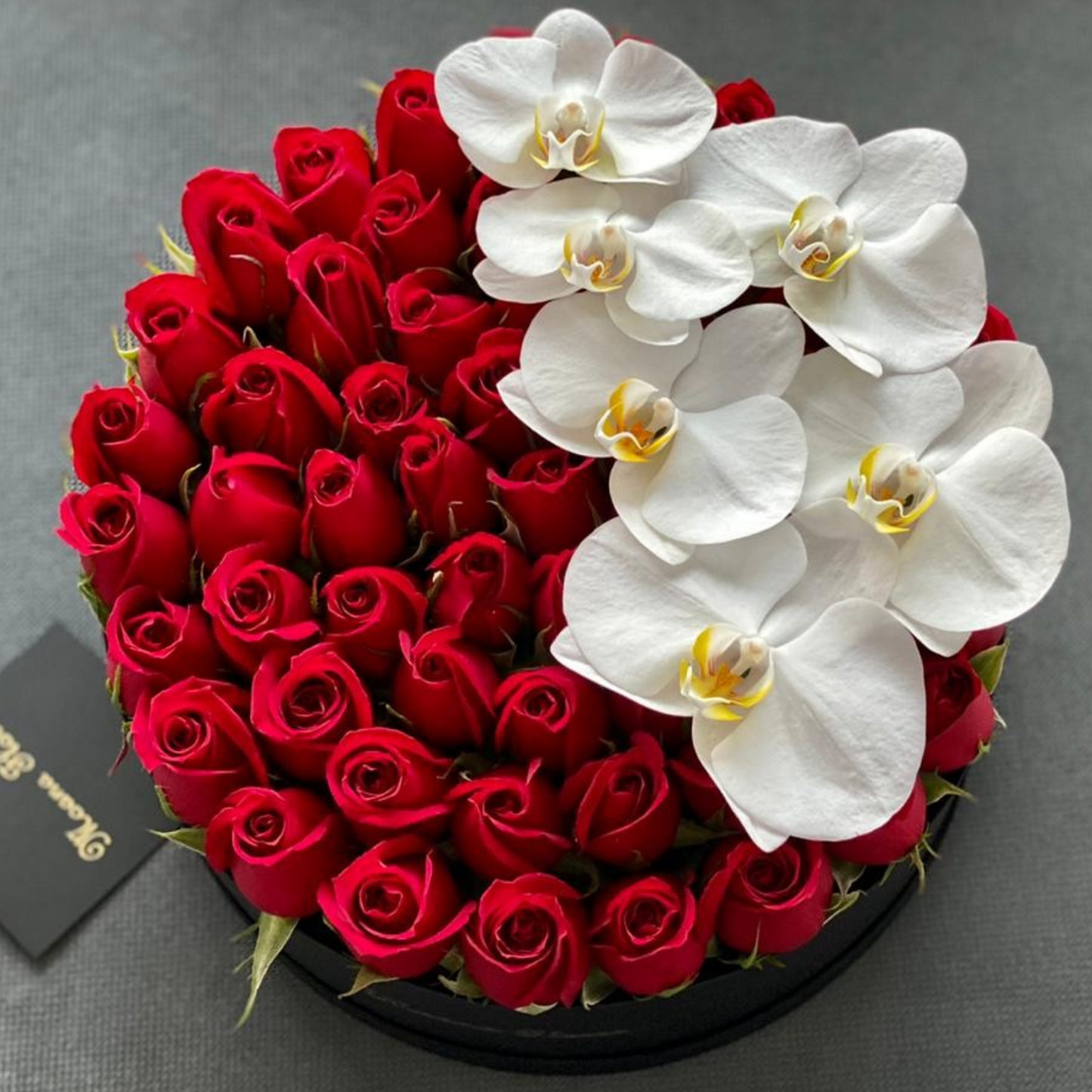 Rosas rojas con orquídeas blancas en caja circular negra.