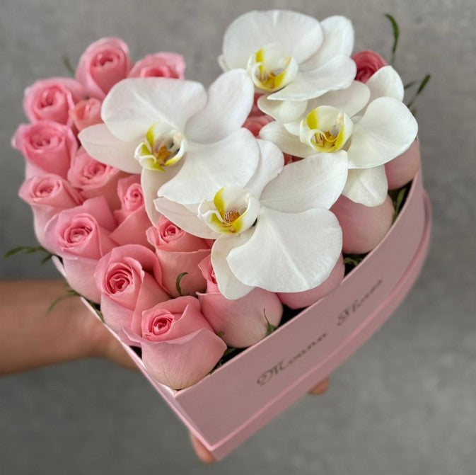 Rosas en tono rosa con orquídeas blancas en caja de corazón.