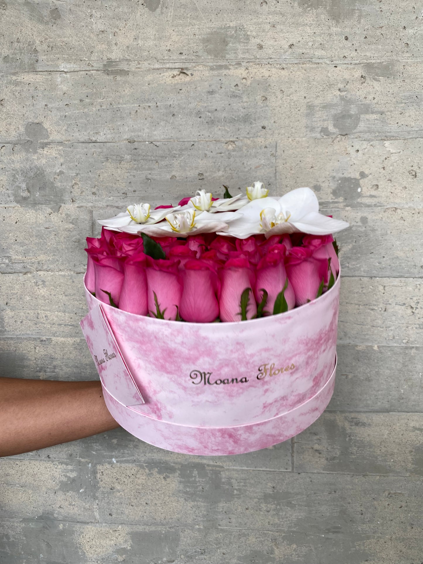 Rosas fucsia en caja de mármol rosa con orquídeas blancas