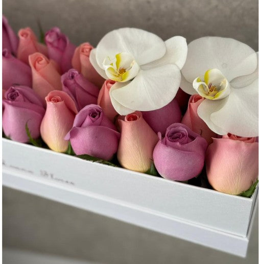 Rosas moradas y hermosas en caja rectangular blanca y orquídeas blancas.
